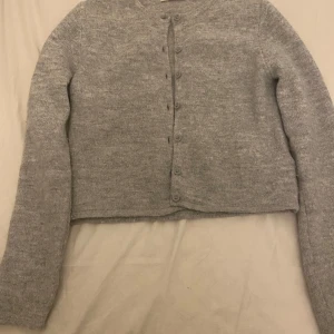 Grå kofta från Gina Tricot - Mysig grå kofta från Gina Tricot i storlek S. Den är stickad och har långa ärmar med knappar hela vägen fram. Perfekt för kyliga höst- och vinterdagar. Enkel och stilren design som passar till det mesta. 🧥✨