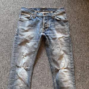 Säljer ett par snygga blå jeans från Nudie Jeans. De har en cool slitning på knäna och en klassisk femficksdesign. Perfekta för en avslappnad stil och passar till det mesta. De är i bra skick och redo för en ny ägare!