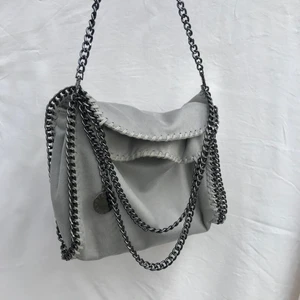 Grå Stella McCartney liknande väska  - En superfin grå Stella McCartney liknande väska med både dragkedja, knapp och 2 olika längder på kedja 🤍 Höjden (uppifrån o ner) är 35cm och bredden (sida till sida) är 32cm ⚡️ Den enda defekten är att knappen är lite sönder på ena sidan, men den går fortfarande att använda 💕 Buda i kommentarerna :) ❗️BINDANDE BUD❗️AVSLUTAS IDAG MÅNDAG 16/8❗️ Kl. 19.00❗️