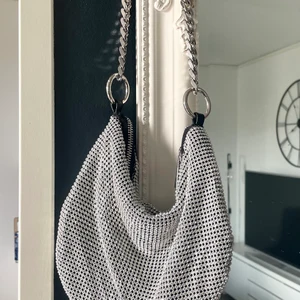 Polly bag - Ginatricot  - Väskan är i nyskick ( aldrig använd ) Väskan är perfekt för festen och silverfärgad och har en axelrem med en kedjedesign. Den har en dragkedja på ovansidan.erfärgad och har en axelrem med en kedjedesign. Den har en dragkedja på ovansidan. mått 22cm x 15cm. Kan skickas köparen står för frakten. 