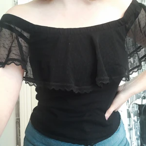Spetstopp - Svart off-shoulder topp med spets och volang. Ganska kort, slutar ungefär vid början av höften. Storlek: Står M men skulle säga S. Material: Polyamid, Spets, Elastan och Polyester. Inga skador.