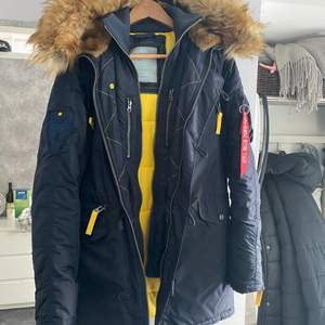 En ny alpha industries jacka, använd fåtal gånger ( ca 5 gånger). Mörkblå med gula detaljer, fejkpäls som går att ta bort. Dubbel knäppning, många fickor, rymlig och skön jacka med snygga detaljer. ✨ Kan skicka spårbart om de önskas, svårt att fastställa exakta fraktkostnad innan försäljning.