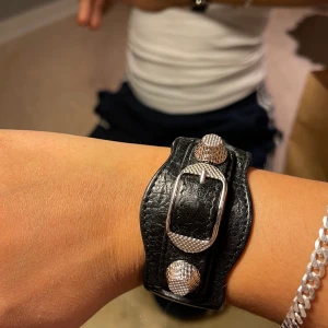 Balenciaga armband - Supersnyggt armband som samlar damm, med nitar från balenciaga deras ”black leather arena giant studed silver bracelet”. Köpt på blocket för 1200kr. Storlek M men justerbar storlek (passa mig med små armleder) sparsamt använt. Lådan och lappar får man med.