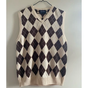 Stickad väst/slipover, S/M - Stickad väst/slipover som passar en stl S eller M. I fint skick. Naturvit botten med bruna rutor och ljusblå ränder. Saknar tvättråd men känns som bomull. Mått: 50cm bred, 70cm lång.