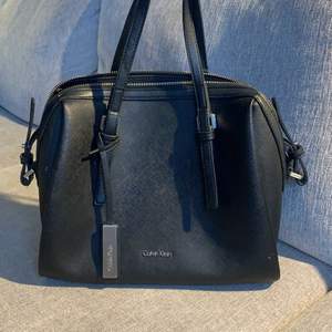 En svart Calvin Klein väska, kommer med ett extra axelband. Använt i cirka 2 år. Dragkedjan är tyvärr trasig men det går att laga! Köpte för 800kr säljer för 300kr