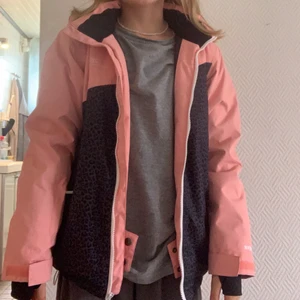 Vinterjacka  - En rosa skidjacka med grå svart Leo mönster. Den har snölås  