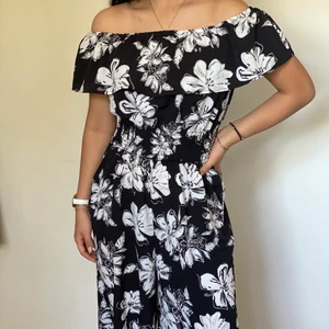 Blommig byxdress  - Lång och svart ’fladdrig’ byxdress med vita blommor. Aldrig använd. Of shoulder med resårband i midjan ich vid axlarna.