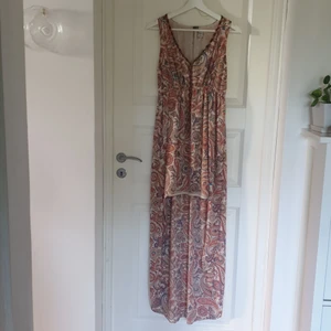 Pepe Jeans klänning st S - Paisley mönstrad klänning i färgerna, beige, korall, ljusrosa och blå. Den är kortare framtill, har v-ringad hals med dekorativa pärlor, underkjol och liten öppning/slits i ruggen. Använd endast ett fåtal gånger. Material polyester. Köpt för 850kr, nypris 1699.