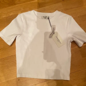 Vit t-shirt från NA-KD - Vit broderad t-shirt från NA-KD. Säljer detta plagg för att den aldrig har kommit till användning.