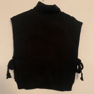 Svart polotröja/väst  - Svart stickad polotröja/väst. Banden vid midjan går att justera då man knyter dem efter önskad passning. Aldrig använd. Storlek L men skulle säga att den är en M, passar S eller mindre L. 