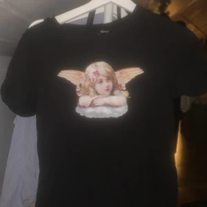Svart tshirt med änglatryck - Söt svart tshirt från hm med ett tryck utav en bokmärkesängel. Storlek xs och knappt använd då den inte riktigt är min stil!💓