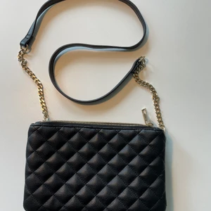 Crossbody-väska - Jättefin crossbody-väska i svart imitationsläder med detaljer i guldkedja och rutigt mönster i tyget. Två stora fack som rymmer mycket. Väldigt bra skick!