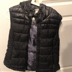 Dunväst med luva  - Dragkejdsfickor, matt tyg nedtill och glansig upptil. Passar mig som är 165, brukar oftast ha Small eller medium i jackor 