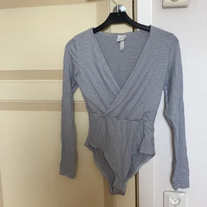 Långärmad randig body H&M - En långärmad, randig body från H&M i blått och vitt. Omlotturringning. Strl S. Knäppning nedtill.