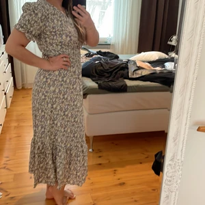 Blommig långklänning  - Småblommig sommarklänning med smock i midjan. Aldrig använd. Pris exkl frakt. 