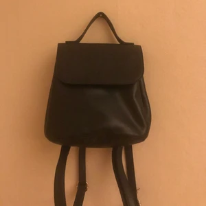 Ryggsäck - Svart ryggsäck i fint skick. Väskan är ganska liten men rymmer de mesta. Den har gulddetaljer. Justerbara band. Man kan även välja om väskan ska vara större eller mindre genom att knäppa två knappar på sidan av väskan. Den har två fack inuti.