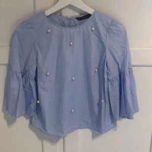 Blus med pärlor från zara storlek Xs - Kortare blus i ljusblått med fastsydda pärlor. 3/4 trumpetärm. Köpt i spanien för något år sedan men har inte använts mer än 3 gånger.