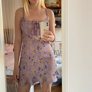 Lila söt klänning - Ljuslila sommarklänning med blommigt mönster i gult, grönt, orange, brunt och svart. Den har en liten volang nertill och en rosett som knyts upptill. Köpt för några år sedan men har endast använt några gånger. Möts i Stockholm annars betalar köpare frakt.