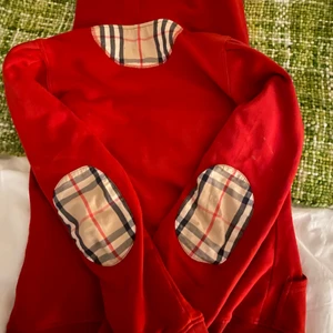 Burberry kofta - Intressekoll på denna röda kofta med patches från Burberry. Den stängs med dragkedja i fram. Kom med egna bud!