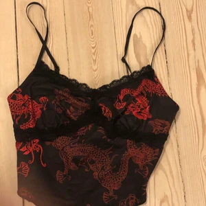 Svart spets topp med röda drakar - Sött Svart spets linne med röda drakar på🐉. Från Shein och har aldrig blivit använd. Helt nytt skick❤️ kan mötas i Stockholm, köpare för frakt annars 💓
