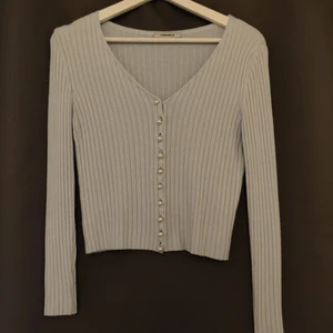 Långärmad tröja med knappar  - Ljusblå tröja med knäppning. Tidigare köpt på plick för 250 kr av en som endast använt fåtal gånger. Själv har jag aldrig använt den. Tröjan är onesized, passar mig som har vanligtvis har M men skulle även passa storlek S. Plagget färg är en klar ljusblå som inte tas upp av kameran