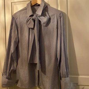 Knytblus från tiger of sweden - Blå och vitrandig knytblus från Tiger i storlek 38. Rymlig i storleken. Blusen har långa manchetter som kan vikas upp över kavajärmarna tex. 