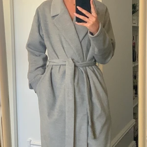 Grå kappa - Grå kappa från Nelly! Råkade klämma bandet i bil dörren vilket syns på bild 2, men är bara smuts så går bort!🤗 (köparen står för frakten)