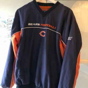 Reebok NFL vindbreaker Chicago Bears - En mörkblå Reebok vindjacka (vindbreaker) från amerikan fotball nfl laget Chicago Bears, väldigt bra skick och bra nu under hösten, den har två fickor på vardera sida samt en liten dragkedja på ena sidan för att lättare trä på sig den. Skriv för fler bilder!