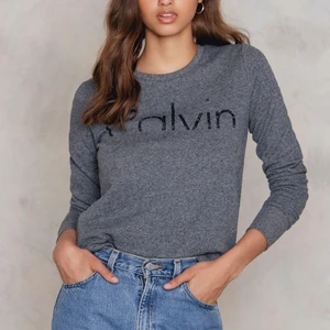 Calvin Klein top - Grå calvin klein jeans sweatshirt med ”halvt” tryck, använd några gånger men inte så att man ser spår av slitningar, köpt på NA-KD, storlek XS!! Skriv privat för fler bilder🥰
