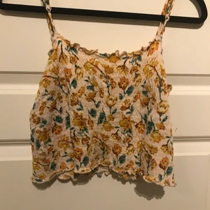 Blommig topp - En blommig smock topp från Urban outfiters. Rosa med gula blommor. Croppad stretchig och bekväm med anpassbara axelband storlek M