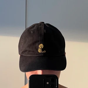 Svart keps med en lite figur - Använd fåtal gånger. Köpt i Korea. Går att byta storlek 