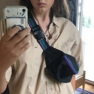 Svart axelväska från Humana  - Svart axelväska köpt på humana second hand. Den har ett stort fack med dragkedja och ett lite mindre fack, även det med dragkedja. Dragkedjorna är lila, och den har även andra detaljer i grönt. Möts gärna upp i Stockholmsområdet, men kan frakta. Köparen står för frakt! 💕