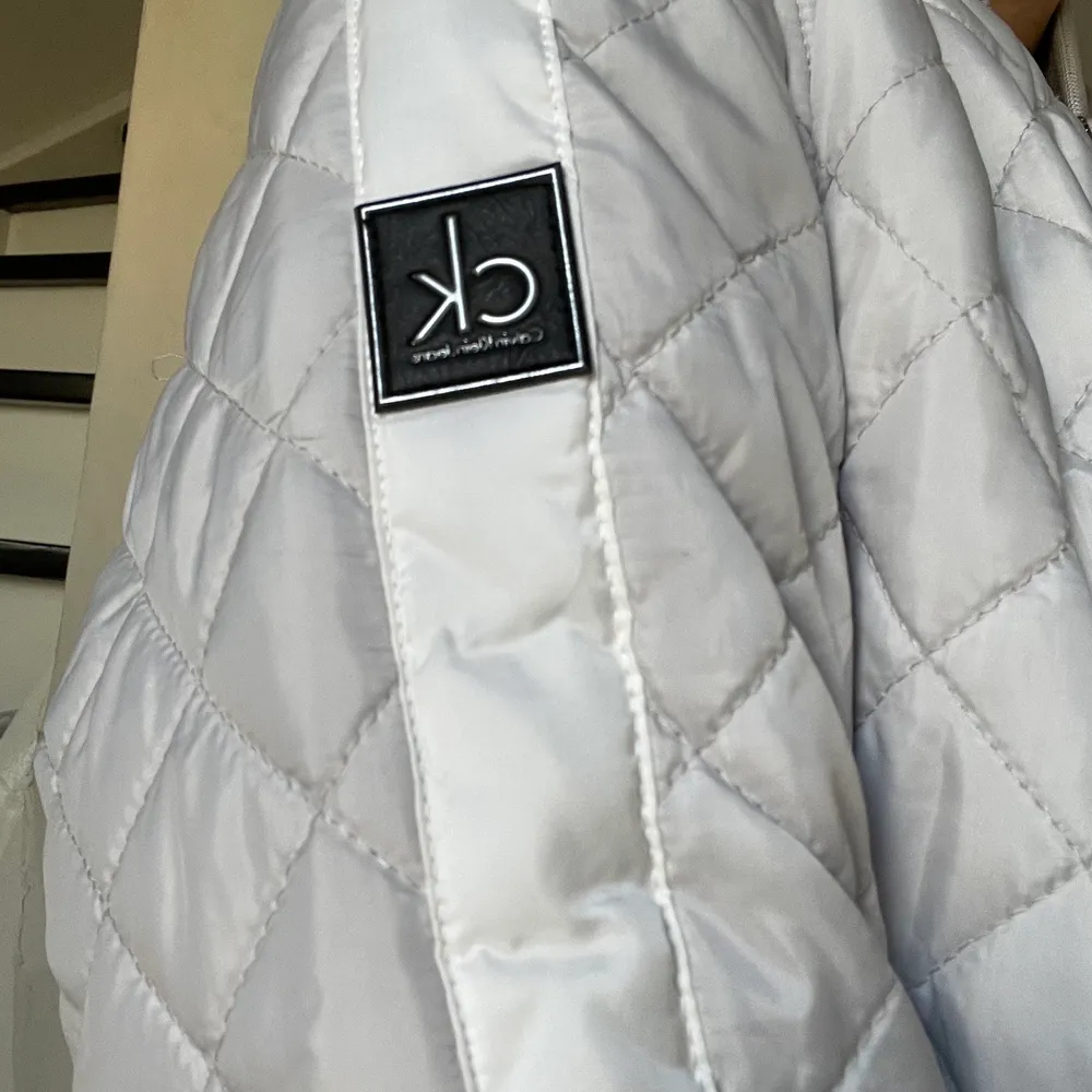 Tunnare dunjacka från Calvin Klein jeans i en silver grå färg med vita detaljer! Helt oanvänd, orginalpris 2000kr. Takit.