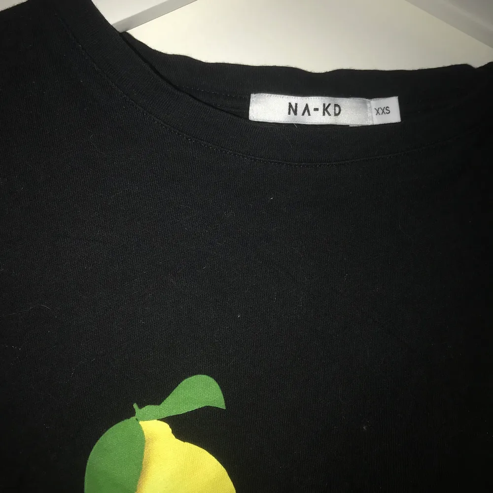 En svart NA-KD t-shirt med citroner på varsin sida av brösten. Stor i storlek, skulle säga att det snarare är en S. . T-shirts.