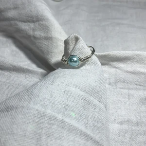 Hemmagjord ring  - En hemmagjord ring med silverfärgad metal och har en liten blå pärla på. Fin att ha till mycket.
