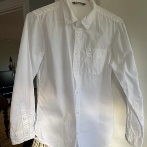 Vit skjorta från Lindex, storlek EUR 146  - Fint skick då den knappt är använd. En ficka där fram med en liten fågel som detalj. Vita knappar längst ner på armarna och på framsidan av skjortan. 