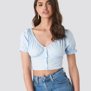 NA-KD topp - Somrig ljus blå top / blus från nakd i storlek 38. Knappar i mitten där fram och resår runt armar och urringning.