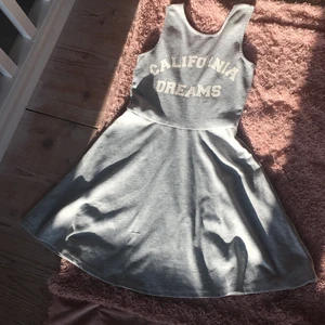 Grå klänning me text. - Detta är en grå klänning med ett tryck där det står (California dreams).Den är i ett väldigt mjukt material och har axelband som är 6cm i bredd och längden är 78cm.