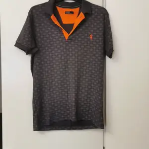 En grå Polo( Ralph Lauren) T-shirt med oranga prickar. Köptes för 2 år men har inte används sedan de första 3 månaderna efter köpet. T-shirten är k storleken L. 