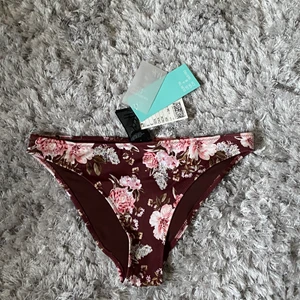 Bikiniunderdel - Jag säljer nu en helt oanvänd bikiniunderdel i storlek 36.😋 Alla lapparna sitter kvar, säljer pågrund av att den är förliten:) Passar superbra med en svart eller vit överdel. Vinröd med blommor i rosa och vit. ☀️😚