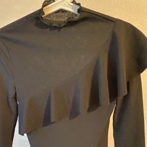 Svart elegant tröja med volang Strl S - Vanlig svart långärmad tröja ribbad, har skönt men finare material som är stretchigt och ger finare sofistikerade vibbar. Har en volang framtill och har något högre hals, knappt använd och är i helt nytt skick. Fler bilder finns om önskas. Jag är i större M därav passar den ej mig fat än den är så töjbar, den passar S 
