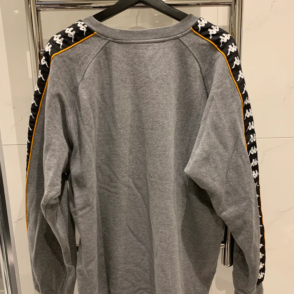 Oversized grå sweatshirt från Kappa med orange, svart och vita detaljer på sidan. Aldrig använt den själv men köpt på Humana i Göteborg. Storlek L men passar även andra storlekar beroende på hur man vill att den ska sitta. Pris kan disskuteras, 66kr frakt tillkommer:). Hoodies.