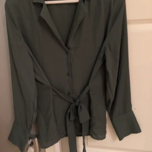 Grön blus med knytning - Så fin grön blus med knytning i fram. Färgen på andra bilden stämmer mer överens med verkligheten! Storlek 40
