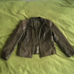 Cool skinnjacka str M - Cool skinnjacka i grönt läder i ormskinnsmönster. Jag säljer den billigare då det finns en fläck bak på ryggen, se sista bilden.
