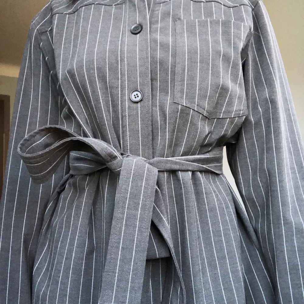 Snygg skjorta från weekday med en kostymkänsla! De tillkommer ett tyg skärp till som man kan knyta runt! Färgen är mörkgrå med vita stripes!. Puvut & Bleiserit.