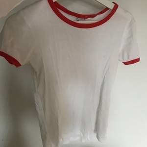 En nice vit tshirt med röda detaljer som har den perfekta längden, inte för lång och inte för kort. Storlek small.