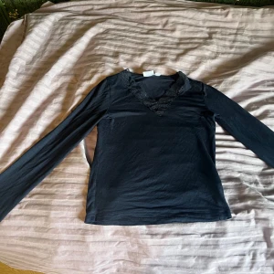 Mörkblå långärmad topp med spets från Gina Tricot - Mörkblå långärmad topp från Gina Tricot med v-ringning och dekorativ spets runt halsen. Tunn och mjuk i materialet, perfekt för lager-på-lager eller som den är. Enkel men med fina detaljer vid halsen. jag har tvättat en gång och haft på mig den en gång