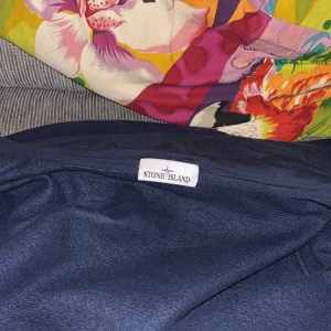 Mörkblå hoodie från Stone Island - Säljer en mörkblå hoodie från Stone Island med dragkedja framtill och klassisk logotyp på ärmen. Hoodien har huva och ribbade muddar. Perfekt för dig som gillar streetwear och vill ha något stilrent.