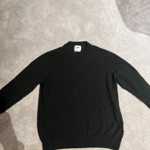 Svart stickad tröja från NN07 - Säljer en klassisk svart stickad tröja från NN07, tillverkad av italienskt garn. Tröjan har rund halsringning och långa ärmar, perfekt för en stilren och enkel look.