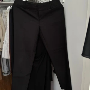 Svarta kostymbyxor från Calvin Klein - Snygga svarta kostymbyxor från Calvin Klein med klassisk passform och hällor för bälte. Perfekta för en stilren look och passar till många olika tillfällen.